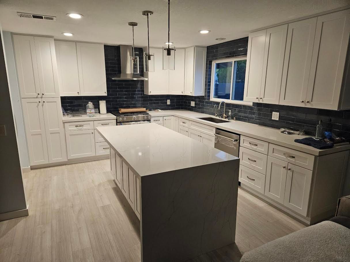 A modern kitchen featuring white cabinets, a large central island with a white countertop, and dark backsplash tiles.