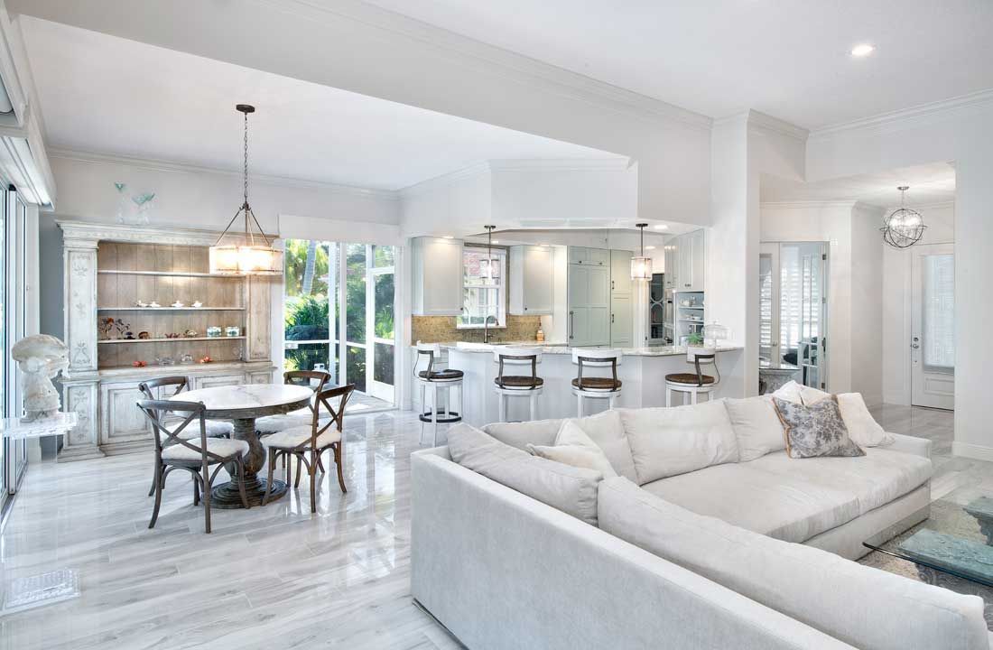 Open-concept living space with white marble floors, a plush sectional sofa, a dining area, and a modern kitchen island.