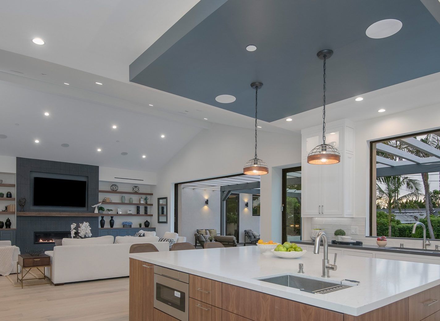 A modern open-plan living room and kitchen featuring a large island, fireplace, and sliding doors to an outdoor area.