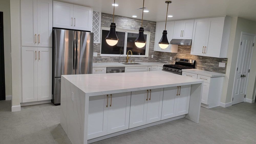 Modern kitchen with a large white quartz island, white cabinets, stainless steel appliances, and stone tile backsplash.