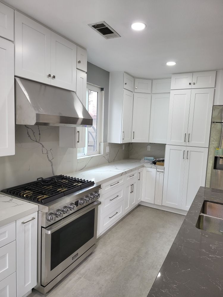 A bright, modern kitchen featuring white shaker cabinets, stainless steel appliances, and a gas range stove.