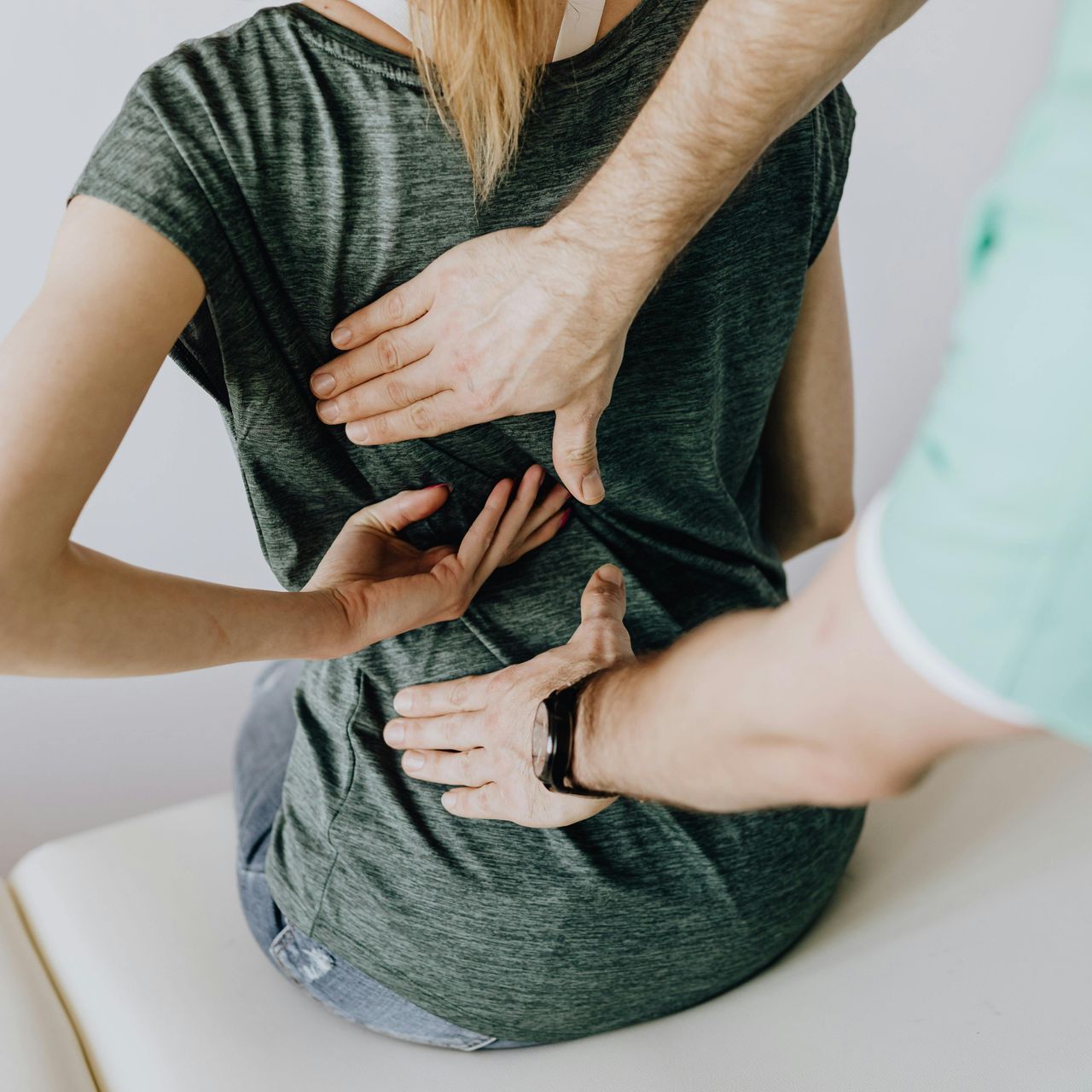 Hands of a medical professional examining a woman's lower back, indicating pain.