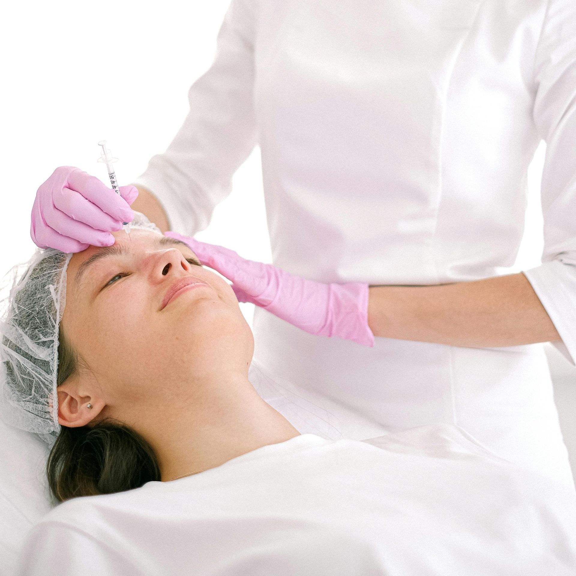 A person receiving an injection to the forehead, administered by someone wearing pink gloves.