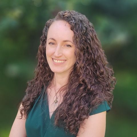 A man in a suit and tie is smiling in front of a brick wall.