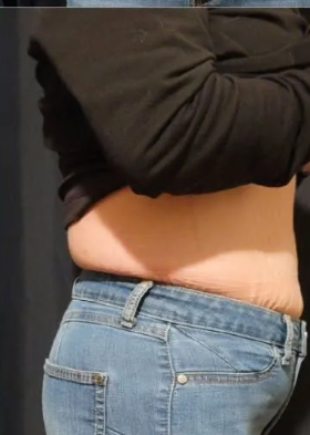 A woman is taking off her shirt and jeans in a dressing room.