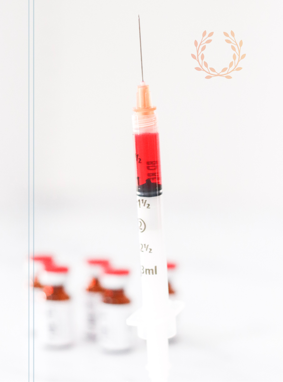 A syringe filled with red liquid is sitting next to a row of bottles.