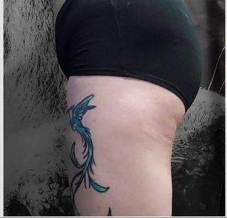 A woman has a blue phoenix tattoo on her side.
