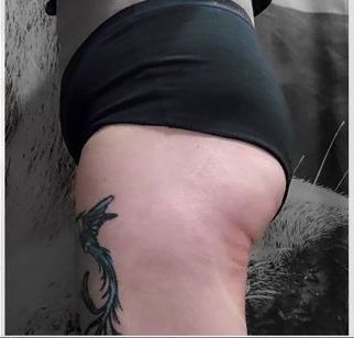 A woman with a tattoo on her leg is wearing black underwear.