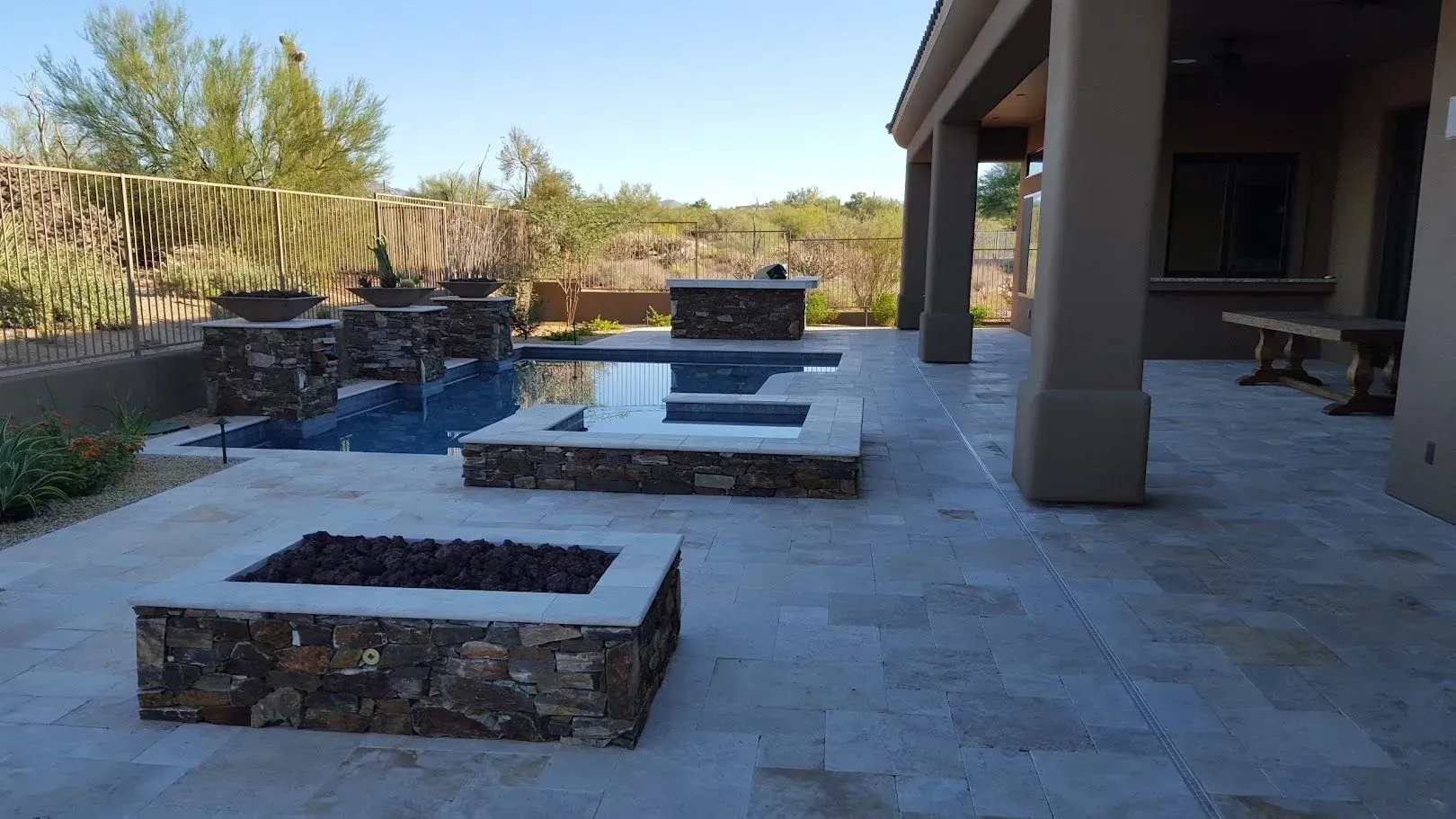 A patio with a fire pit and a pool in the background.