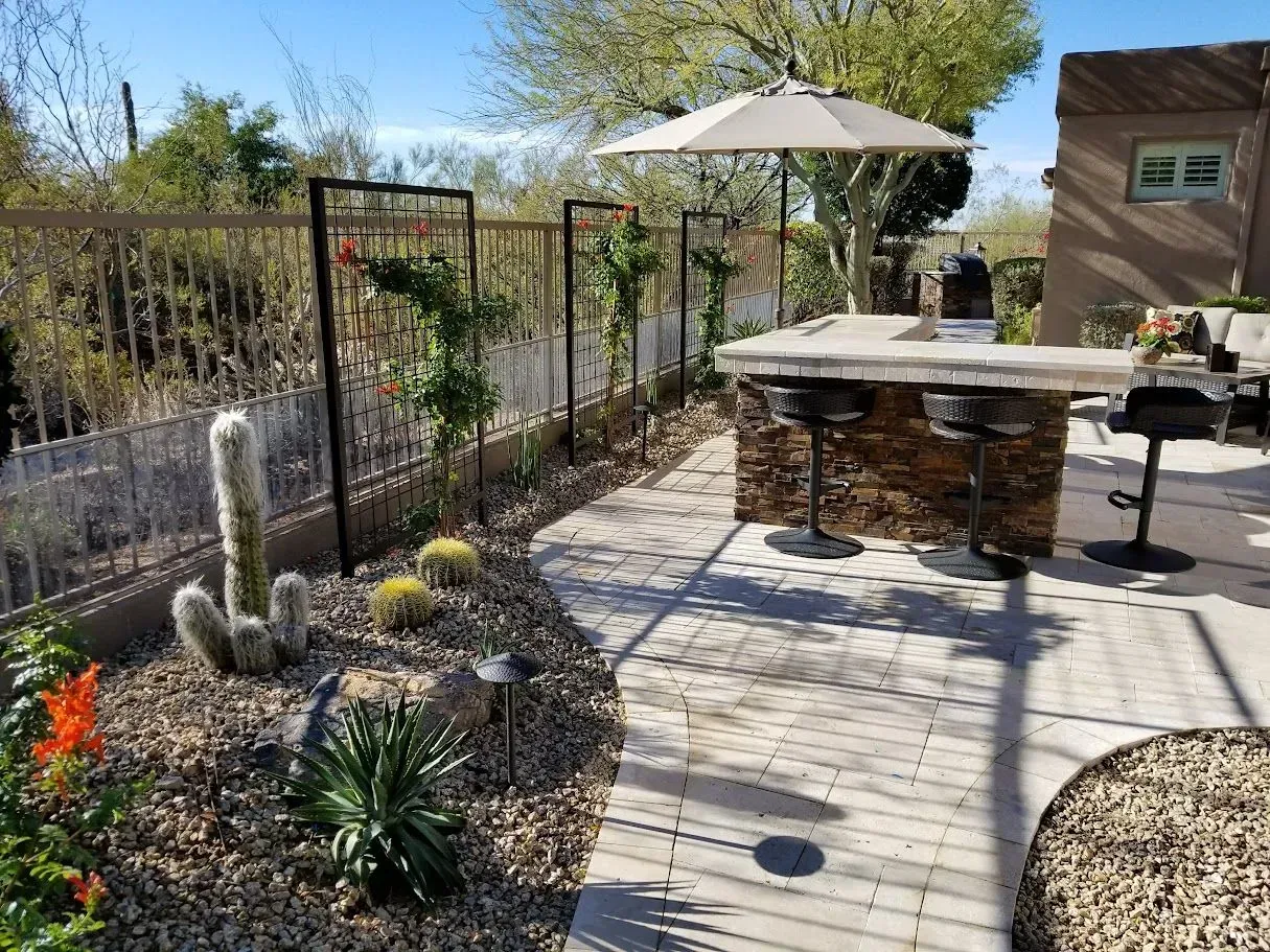 A patio with a table , chairs , umbrella and cactus.