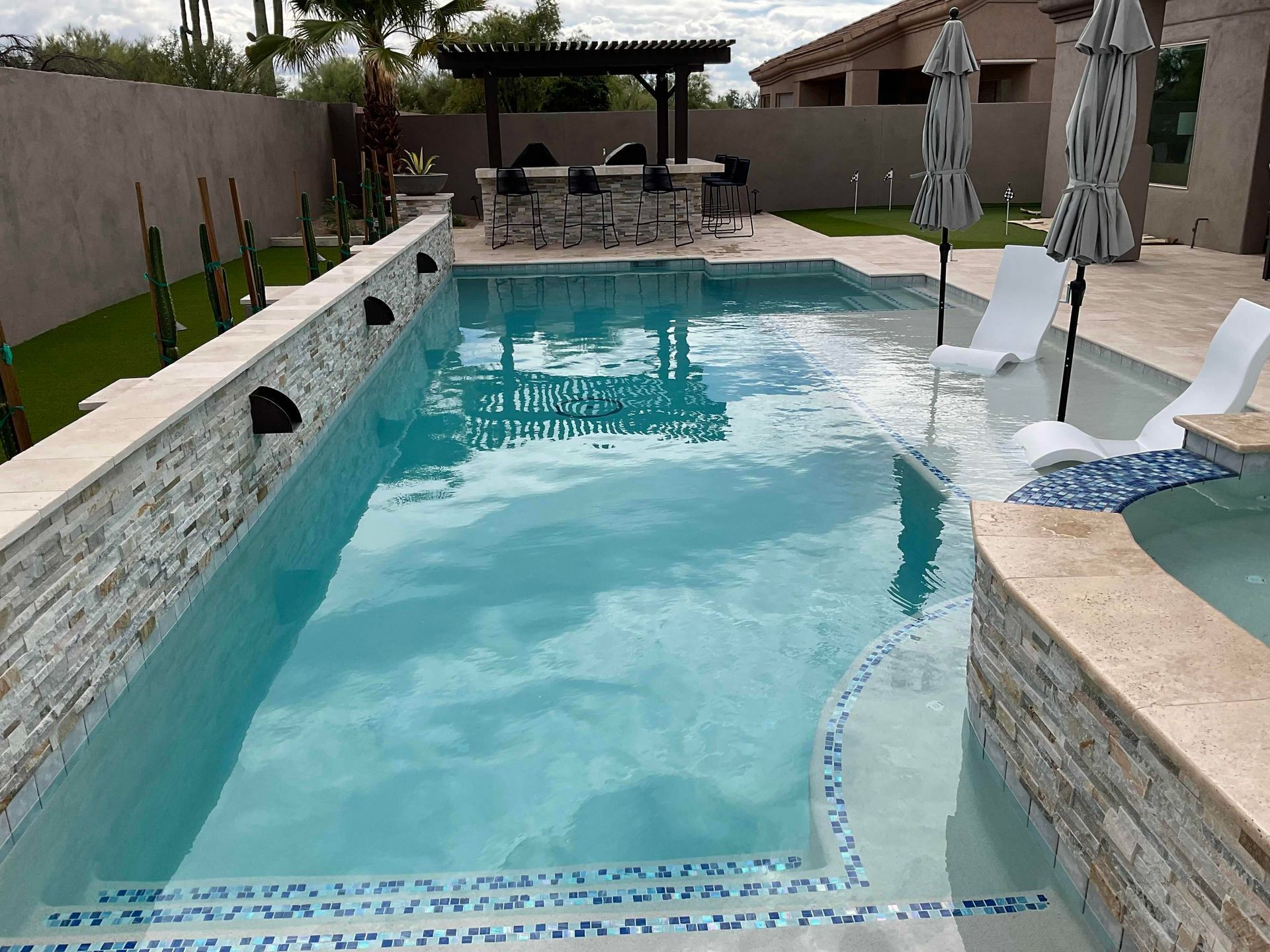 A large swimming pool surrounded by chairs and umbrellas in a backyard.