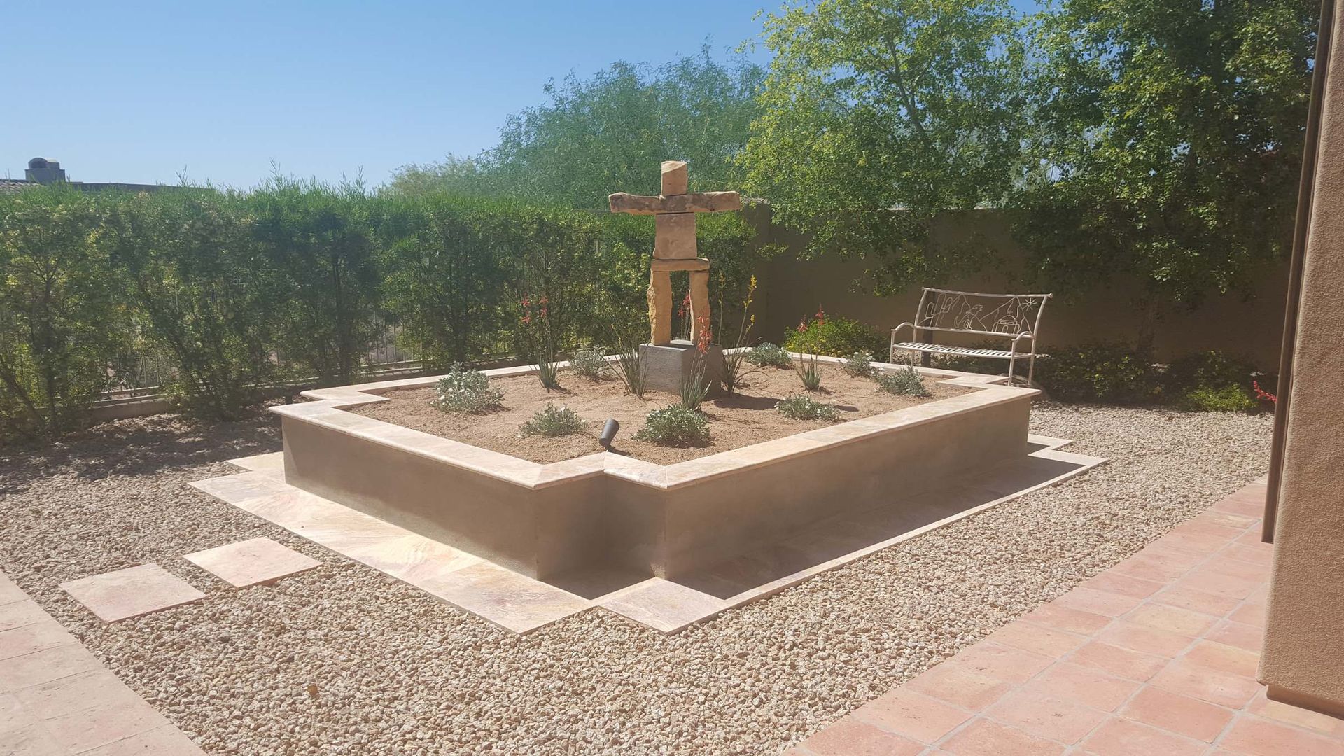 A fountain in the middle of a gravel yard with a bench in the background.