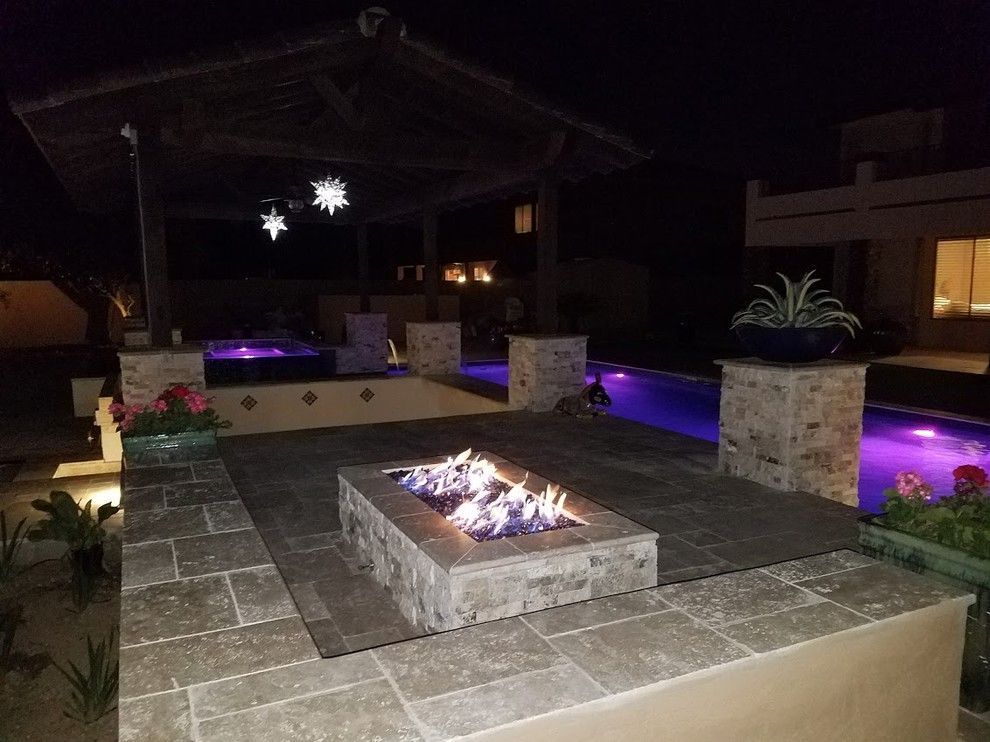 A fire pit in the middle of a patio next to a pool at night.