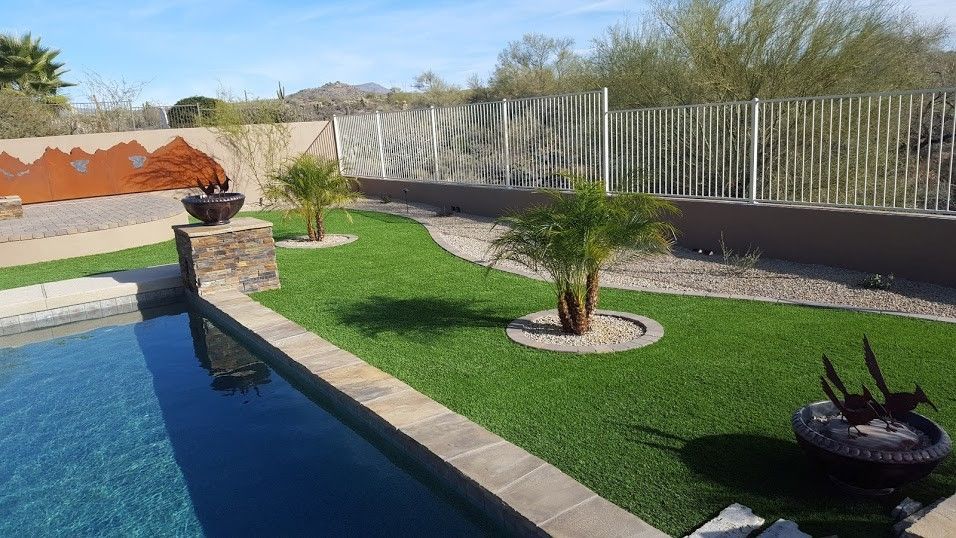 A swimming pool surrounded by a lush green lawn and palm trees.