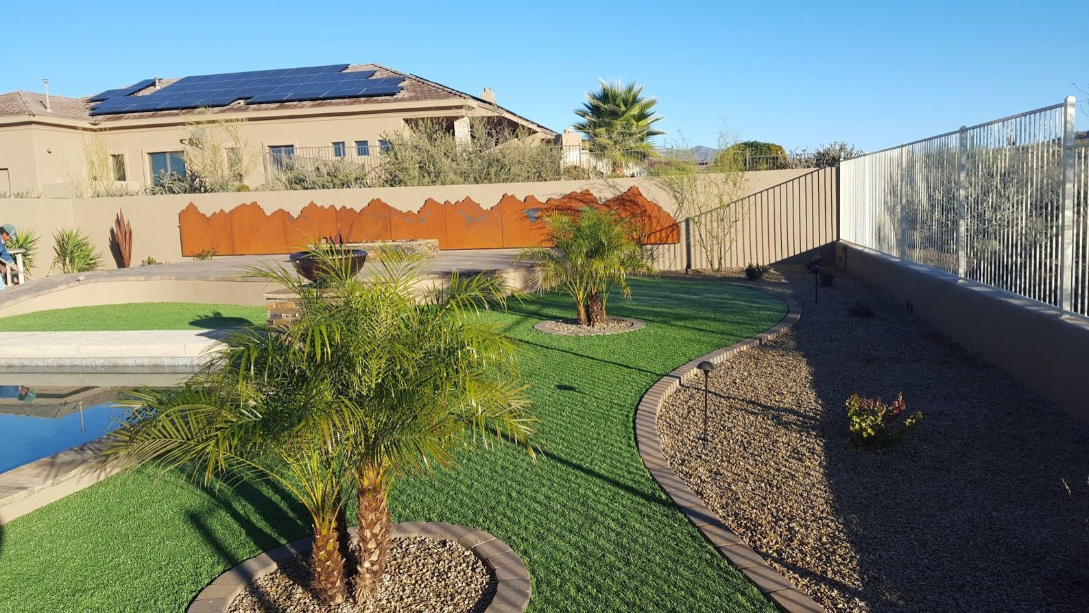 A large house with solar panels on the roof is surrounded by a lush green lawn.
