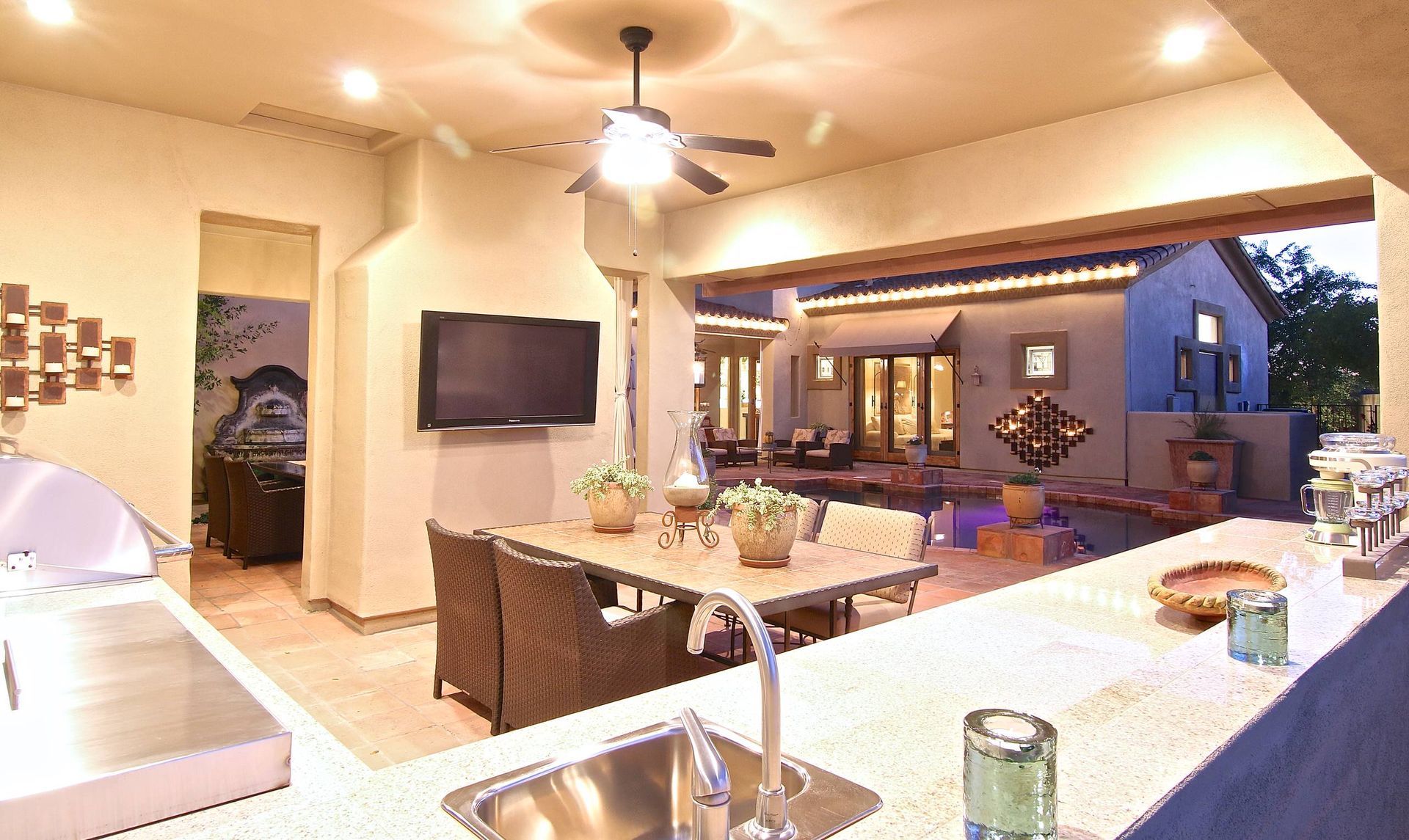 A kitchen with a sink , table , chairs and a flat screen tv.