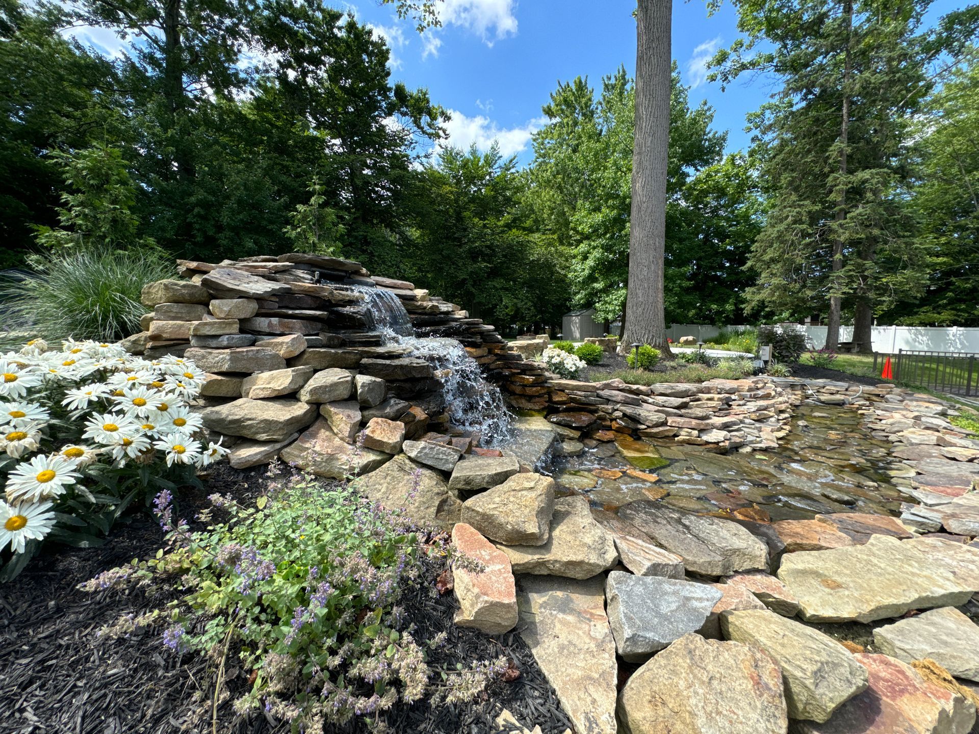 A waterfall is surrounded by rocks and flowers in a garden.