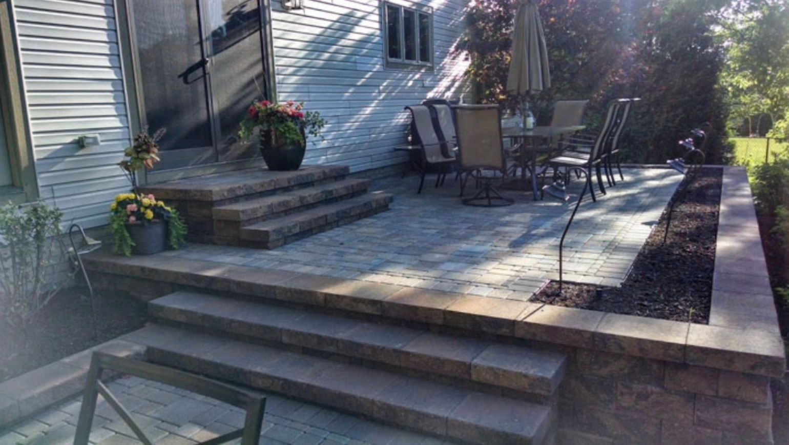 There is a patio with a table and chairs on it in front of a house.
