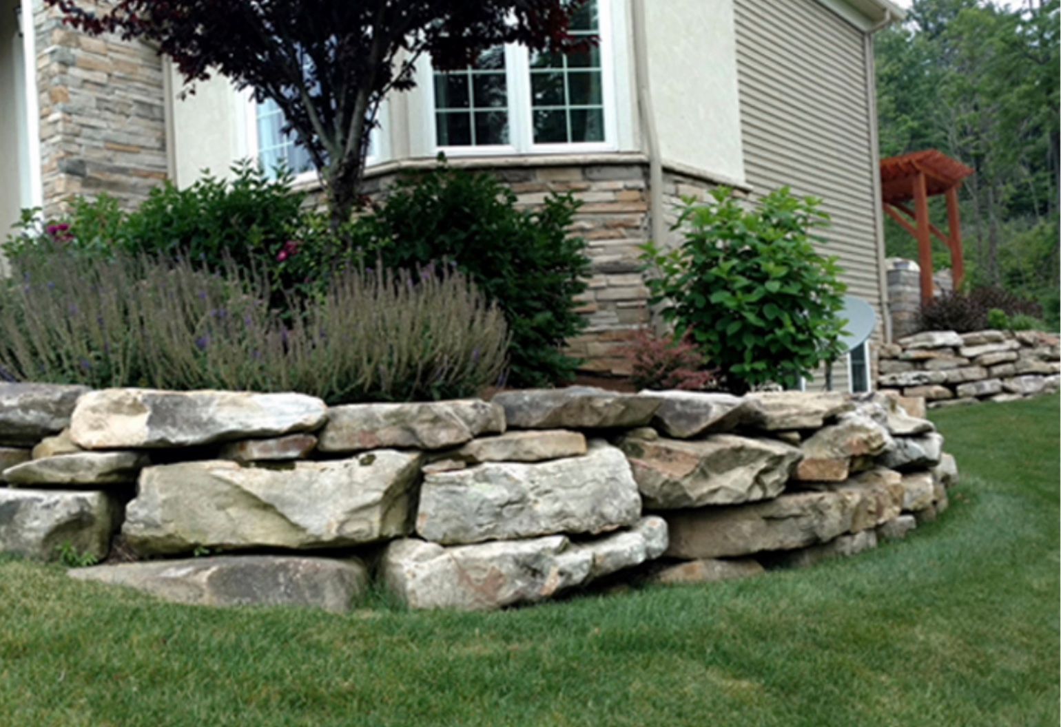 A stone wall in front of a house with a tree in the background.