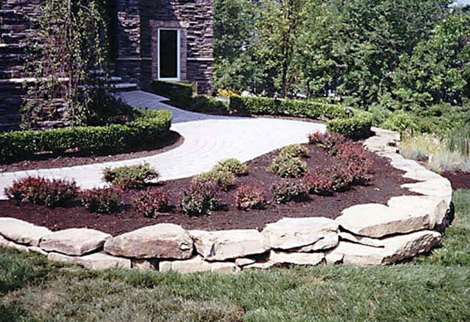 A stone wall surrounds a driveway leading to a house