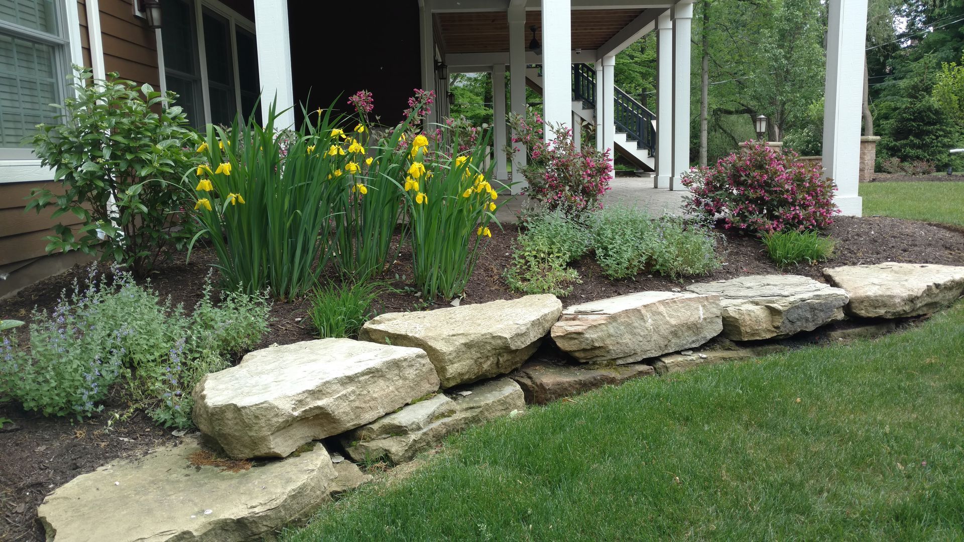A house with a stone wall and flowers in front of it.