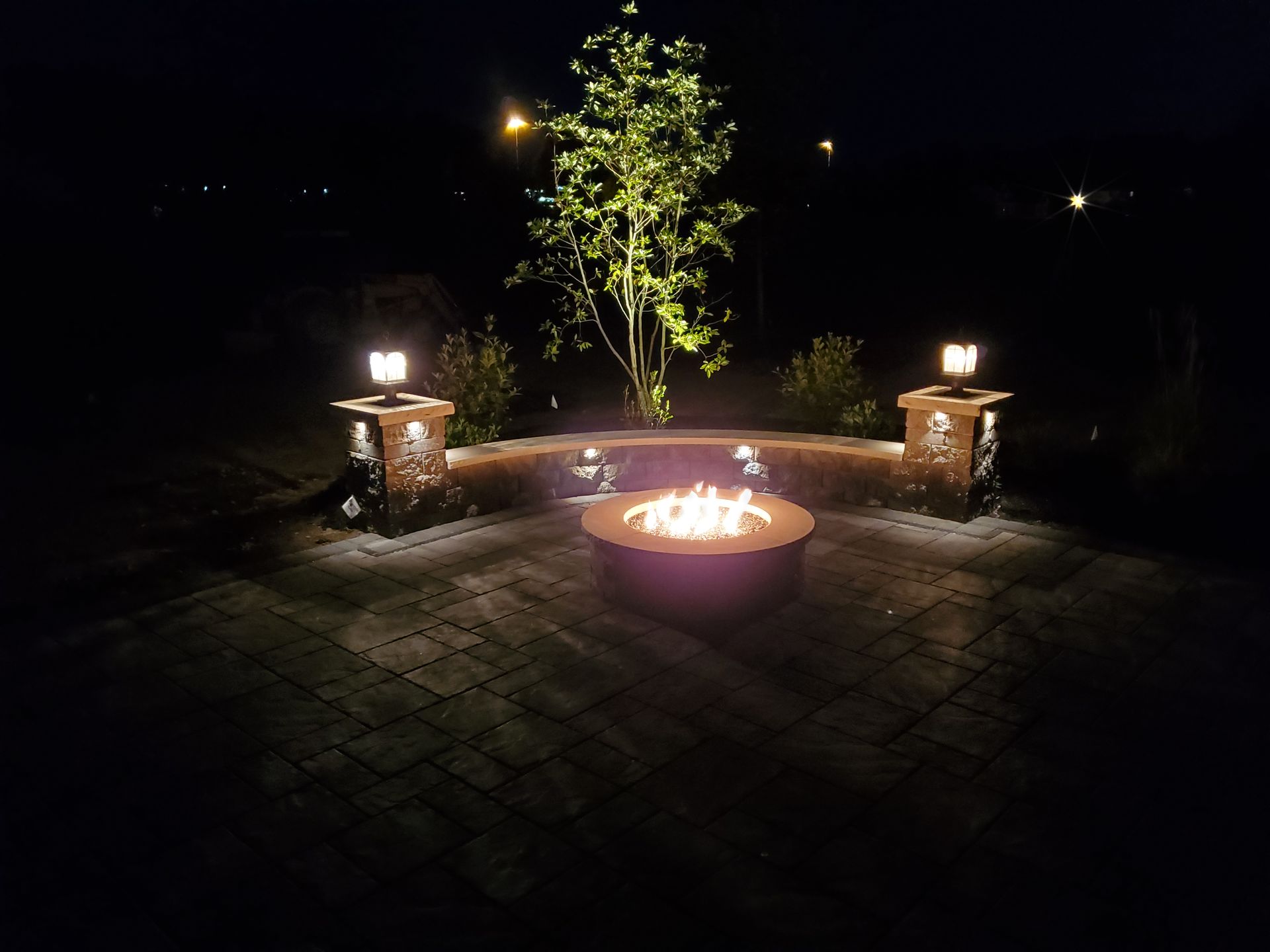 A fire pit is lit up at night on a patio.