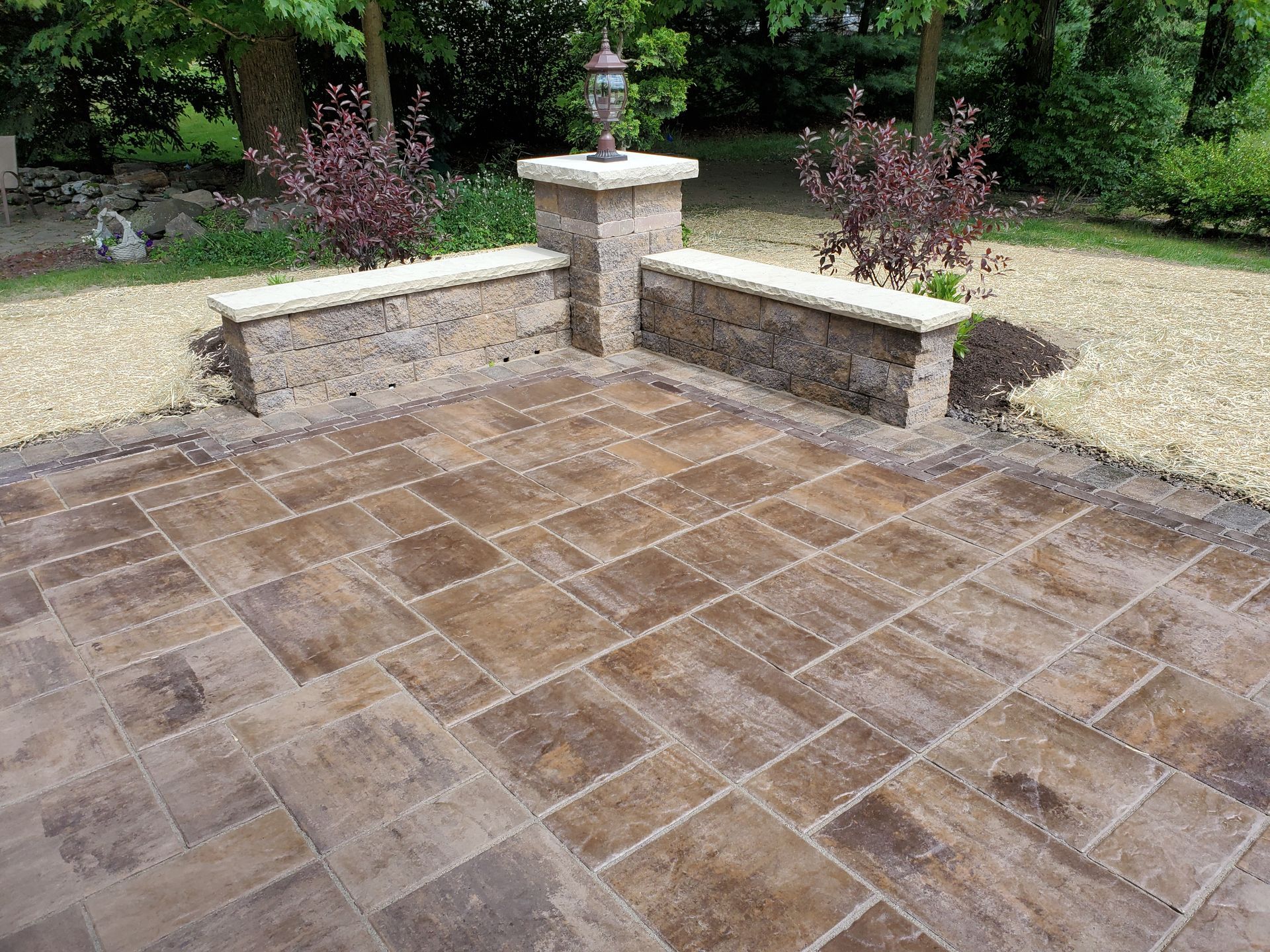 A patio with a brick wall and a bench in a backyard.