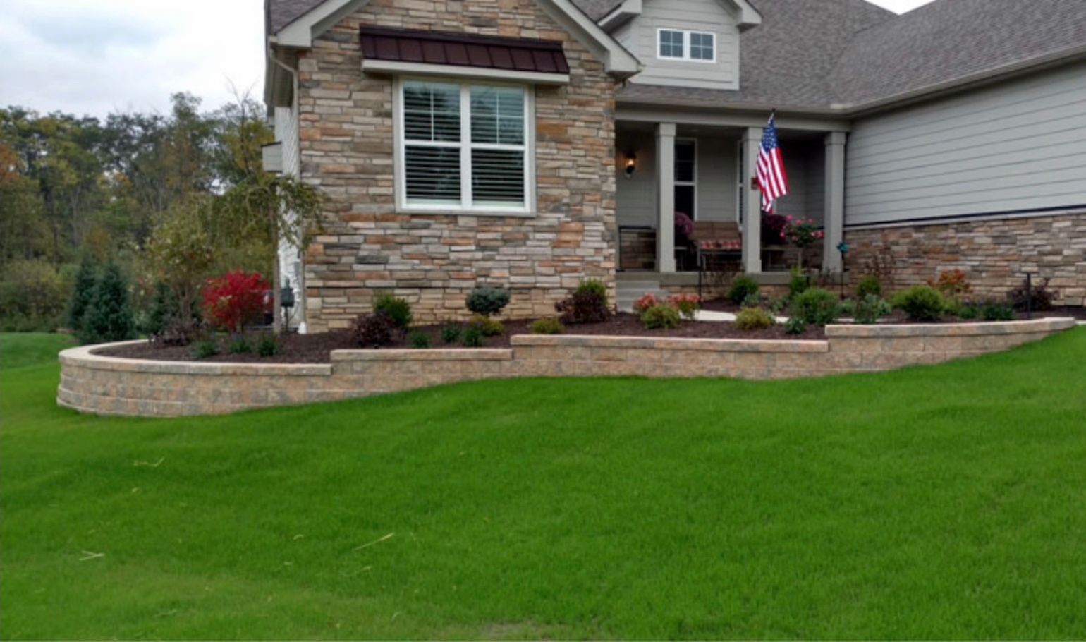 A house with a large lawn and a stone wall in front of it.
