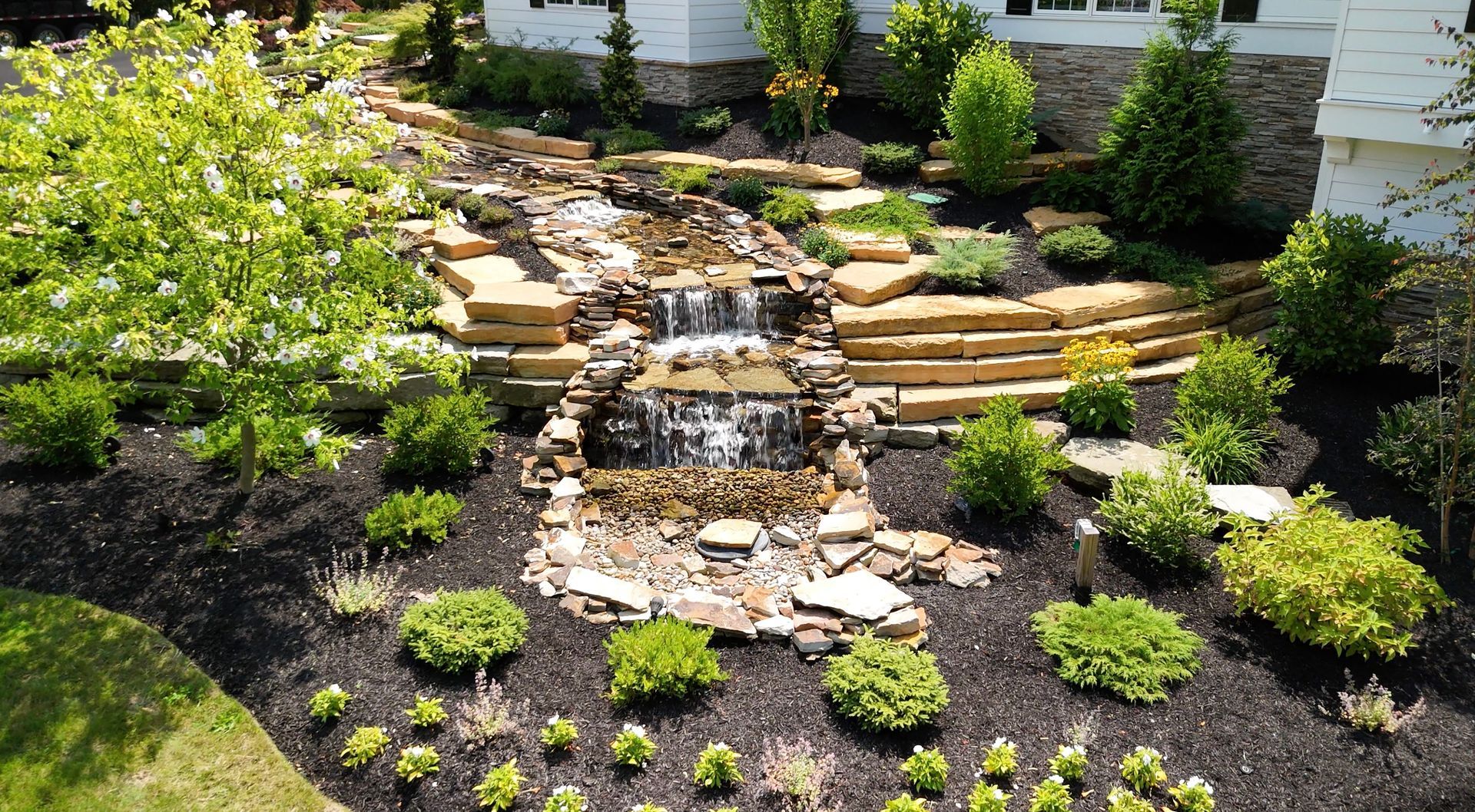 An aerial view of a waterfall in a garden in front of a house.