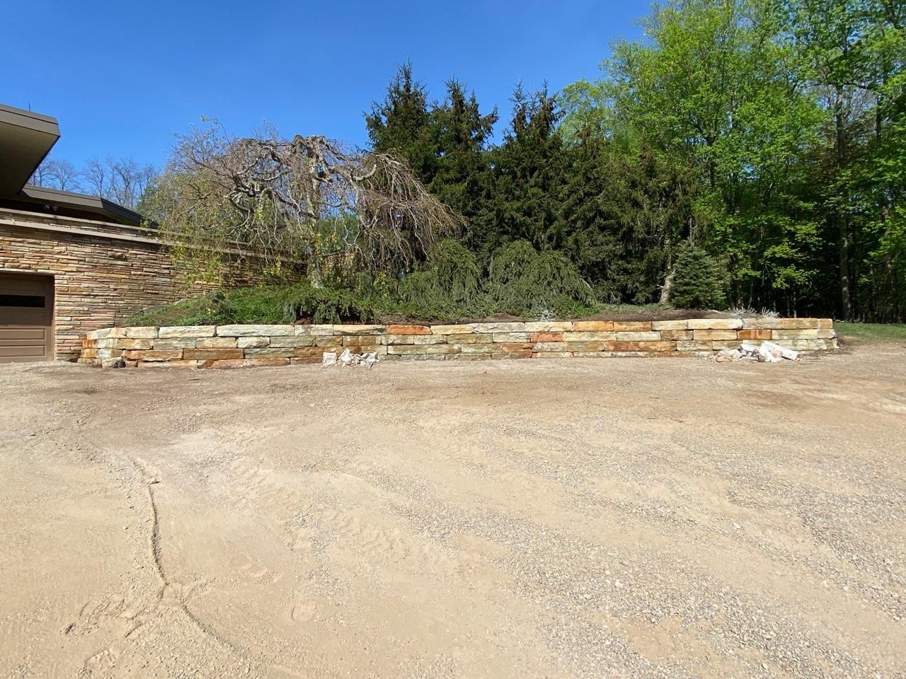 A driveway with a stone wall in front of a house.