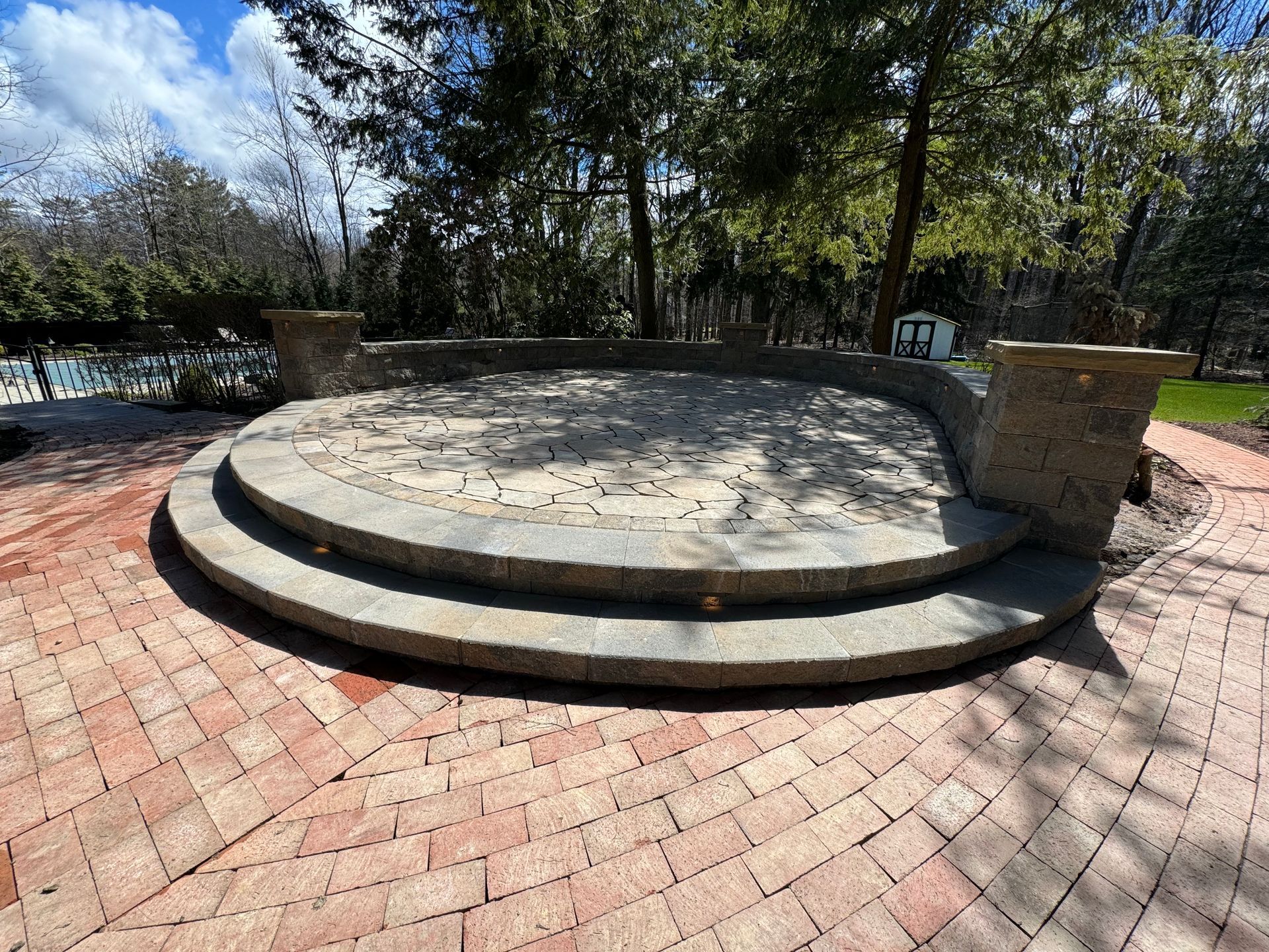 A circular brick patio with steps leading up to it and trees in the background.