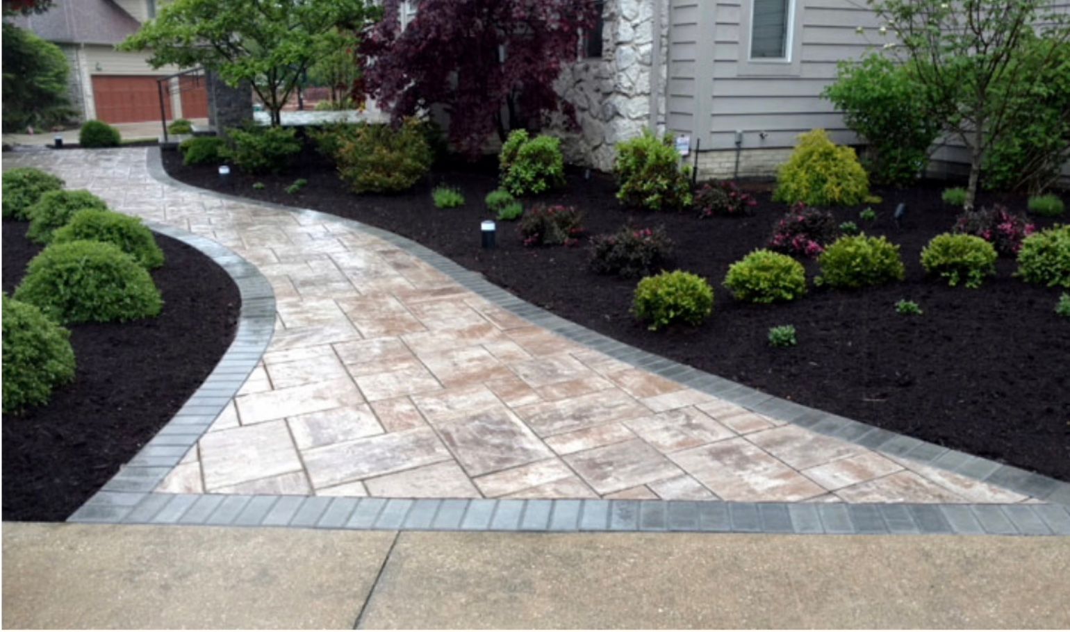 A brick walkway leading to a house surrounded by trees and bushes.