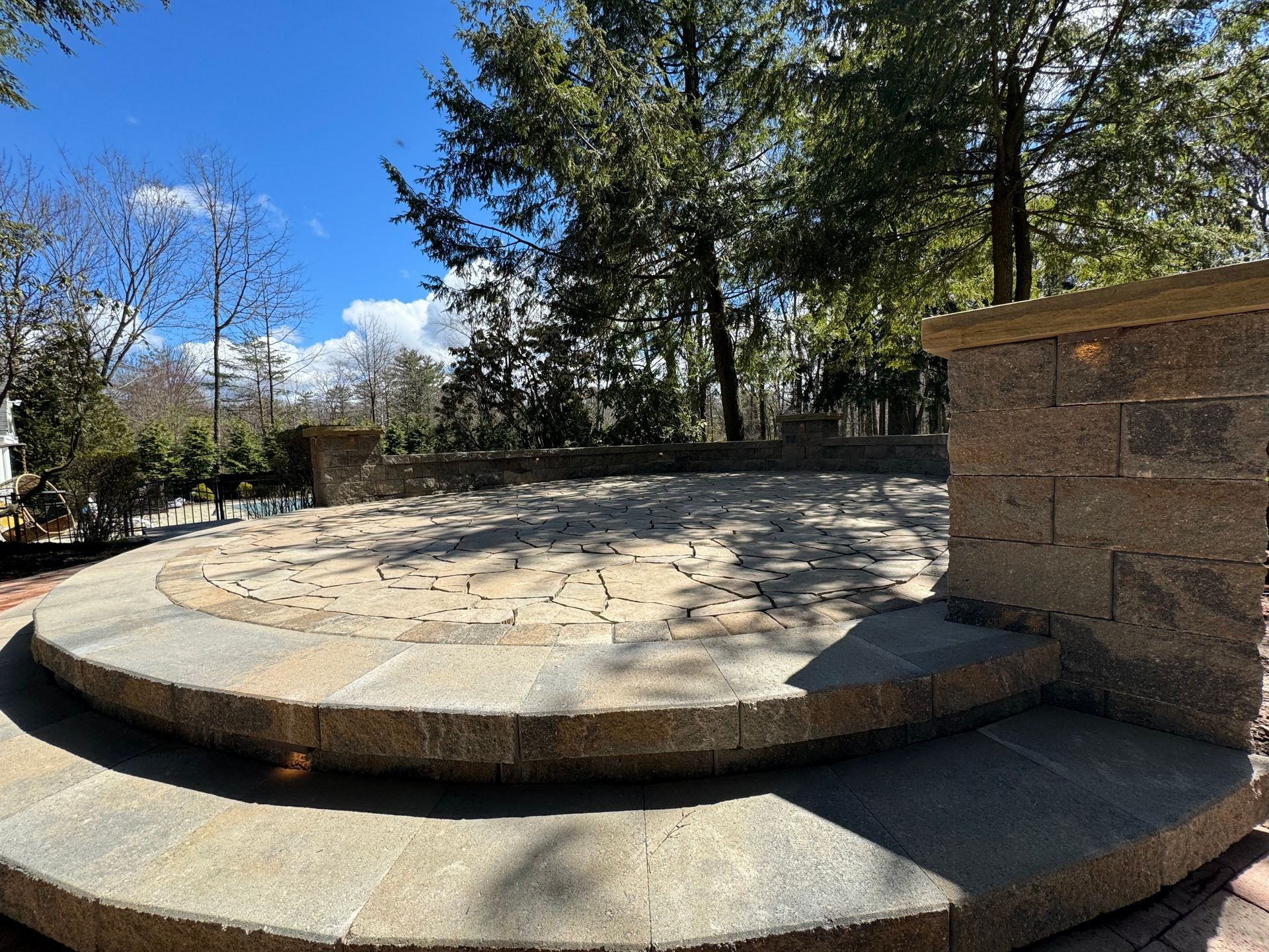 A circular stone patio with a brick wall and trees in the background