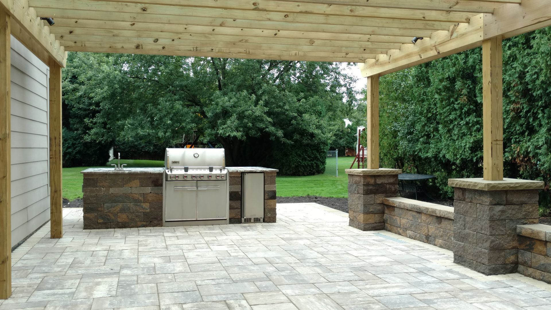 A patio with a grill under a wooden pergola