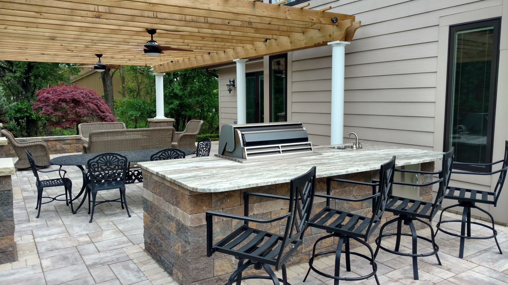 A patio with a table and chairs and a grill under a pergola.