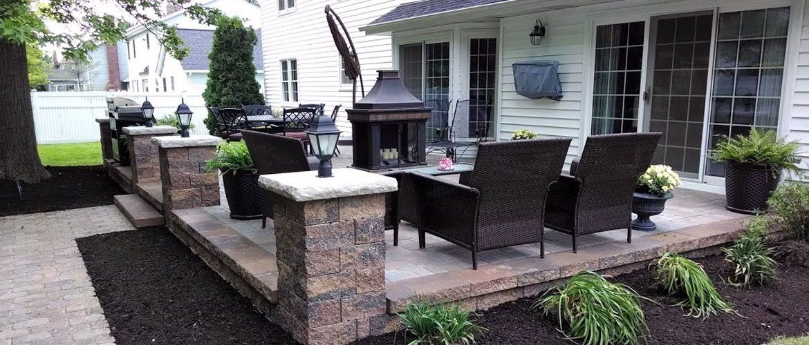 A patio with chairs , tables and a fireplace in front of a house.