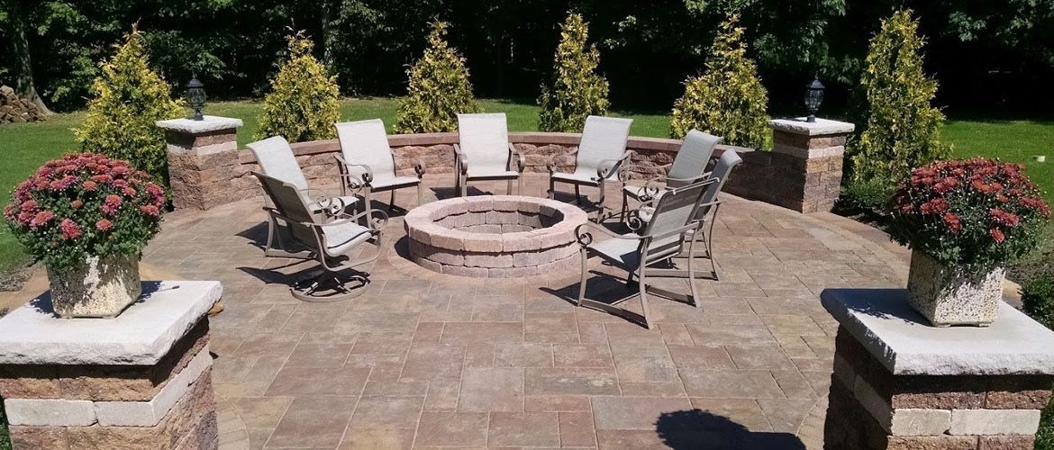 There is a fire pit in the middle of the patio with chairs around it.