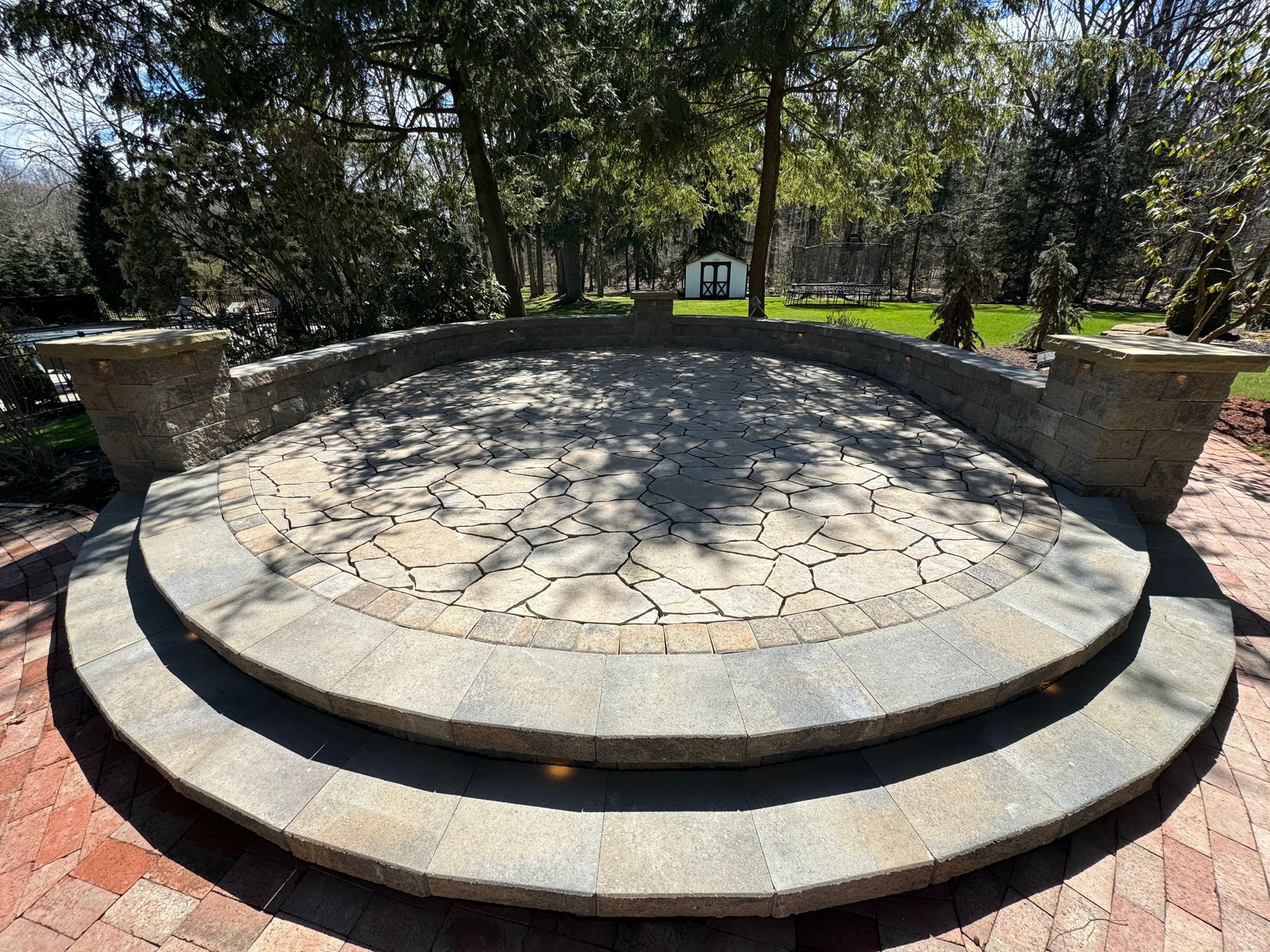 A circular stone patio in a park with trees in the background