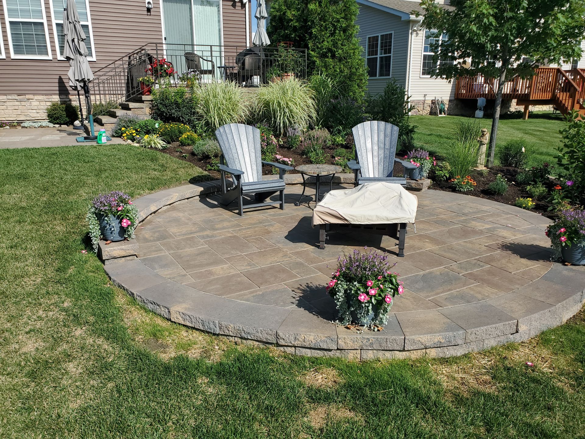 A patio with two chairs and a table in the middle of a lush green yard.