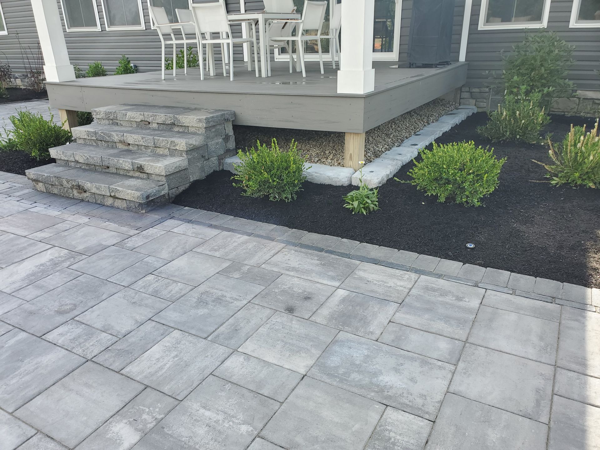 A patio with steps leading to a porch with a table and chairs.