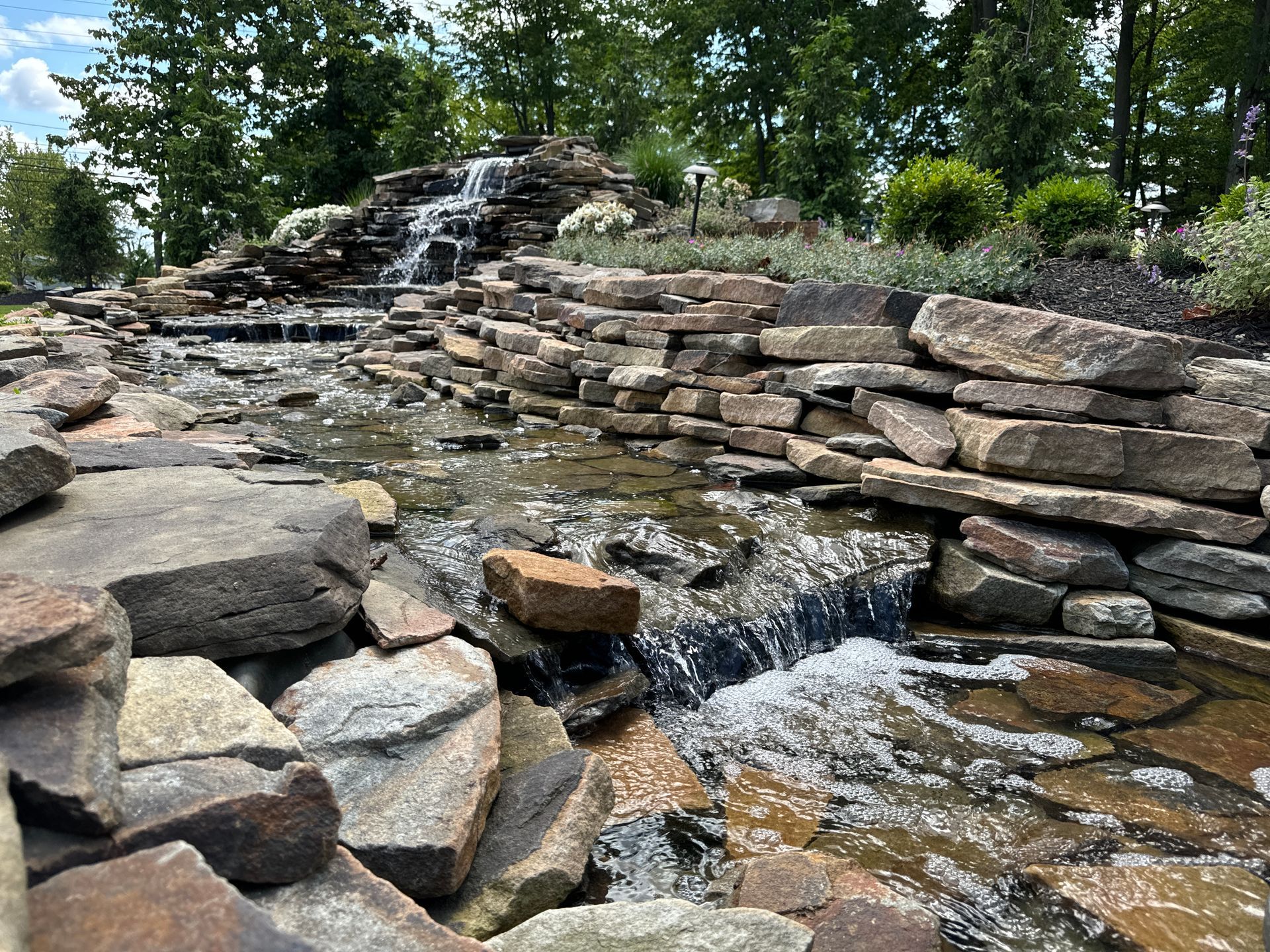 A waterfall is surrounded by rocks and trees in a park.