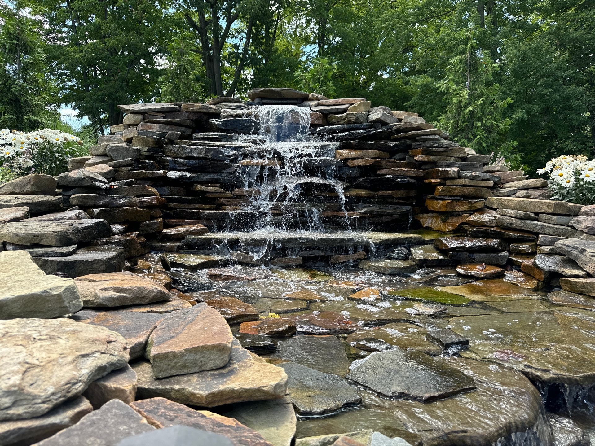 A waterfall is surrounded by rocks and trees in a park.
