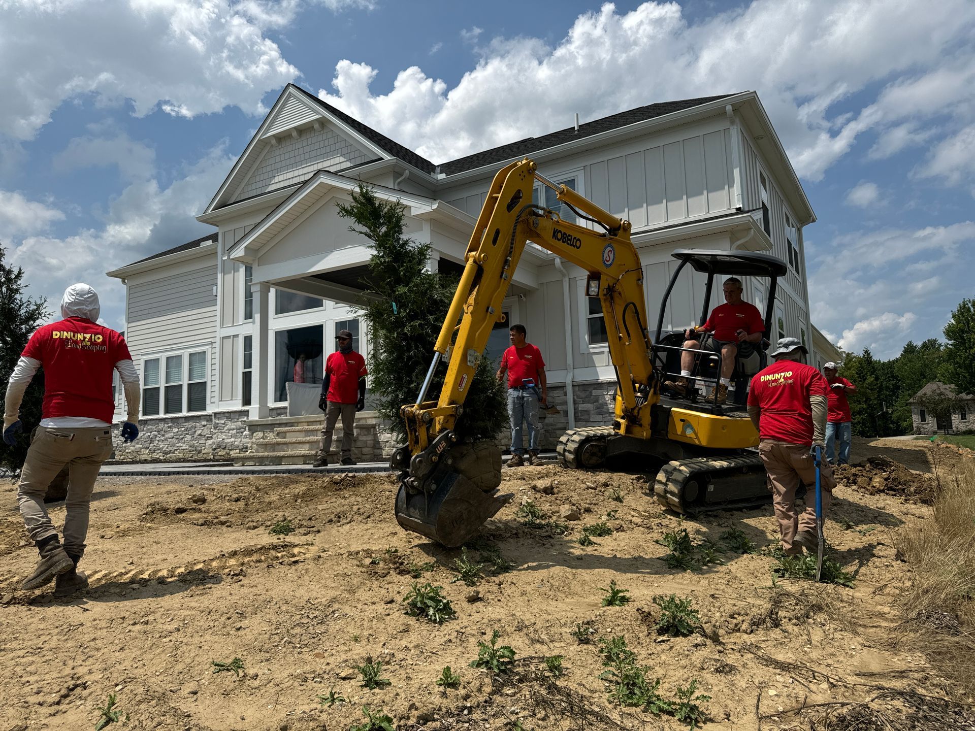 A group of construction workers are digging a hole in front of a large house.