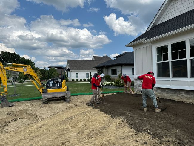 A group of construction workers are working on a driveway in front of a house.