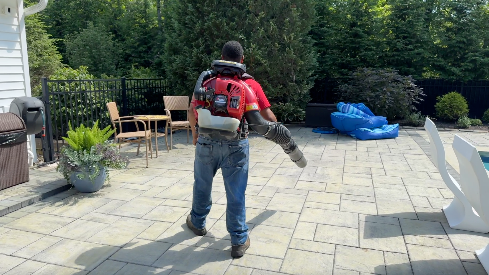 A man is walking on a patio with a backpack blower.