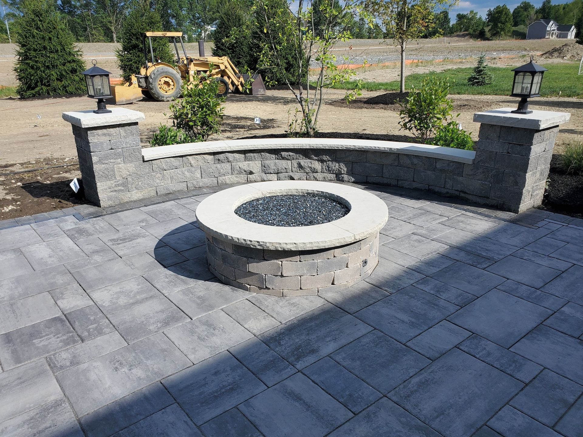 A fire pit on a patio with a tractor in the background.