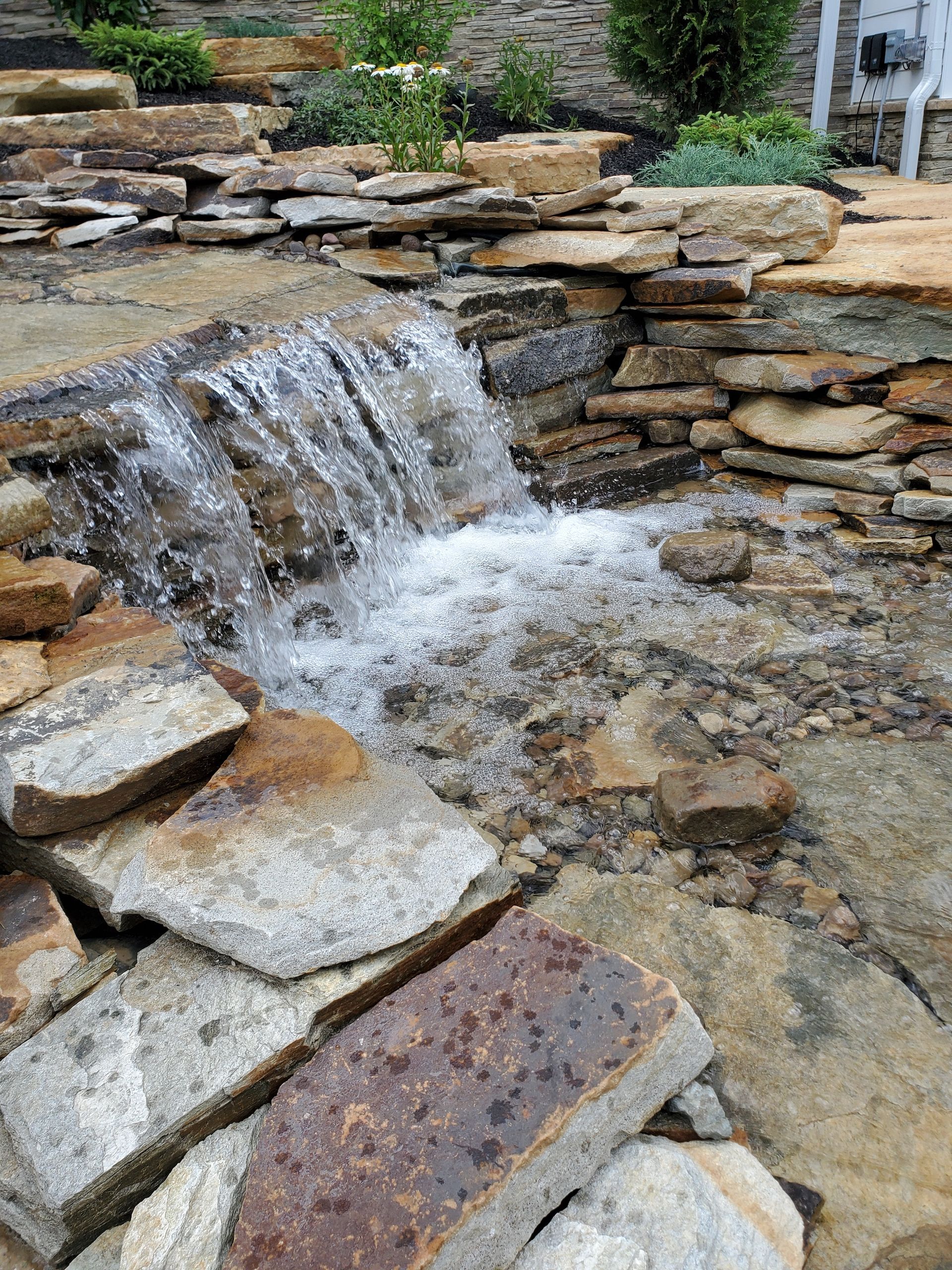 A small waterfall is surrounded by rocks in a garden.