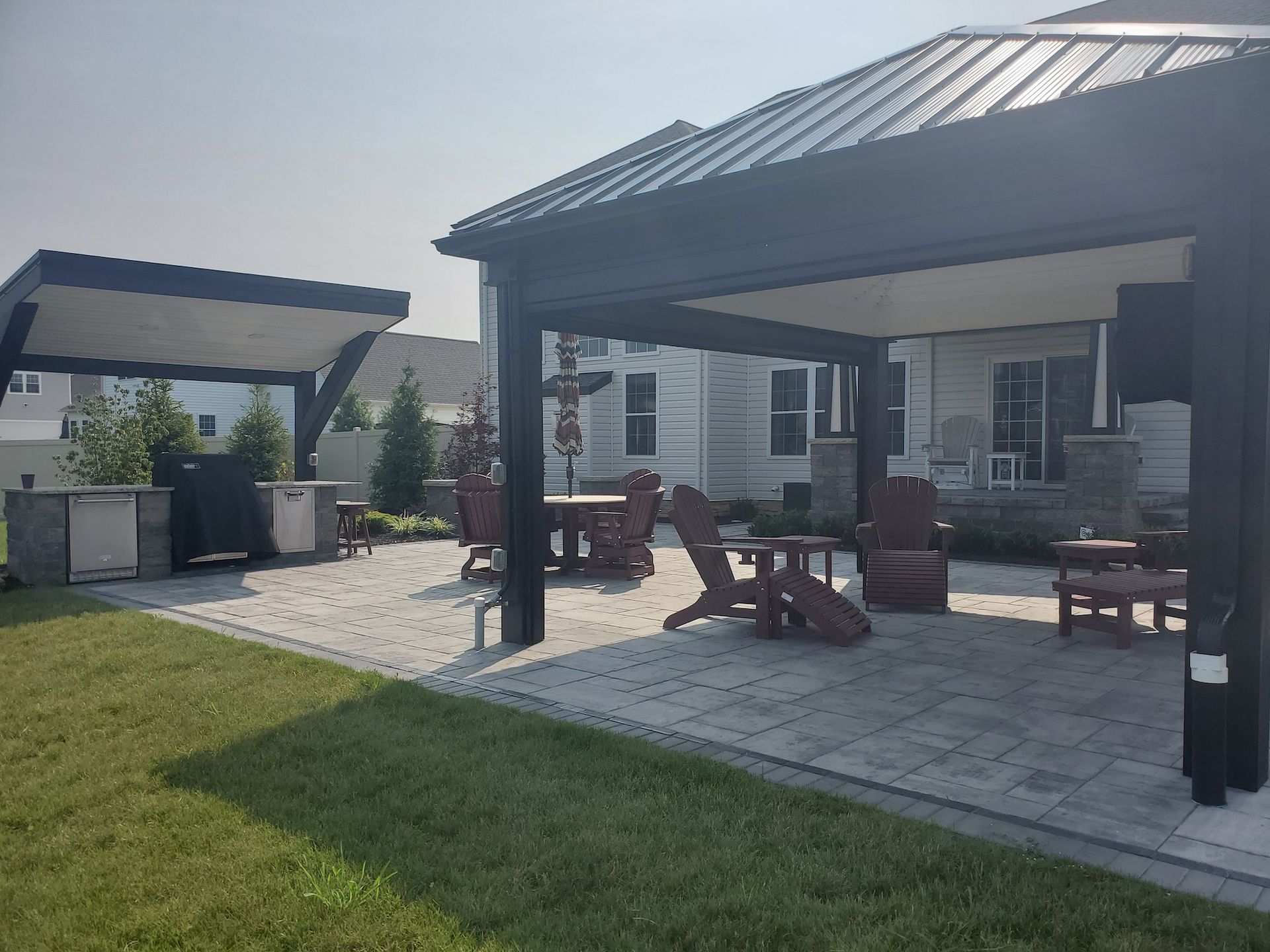 A patio with a table and chairs under a pergola in the backyard of a house.