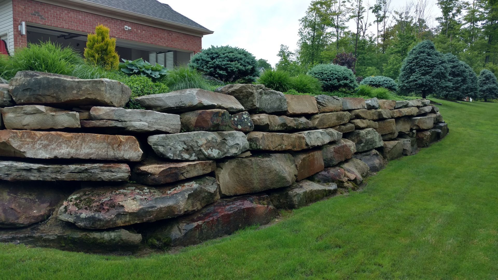 A large rock wall surrounds a lush green lawn in front of a house.