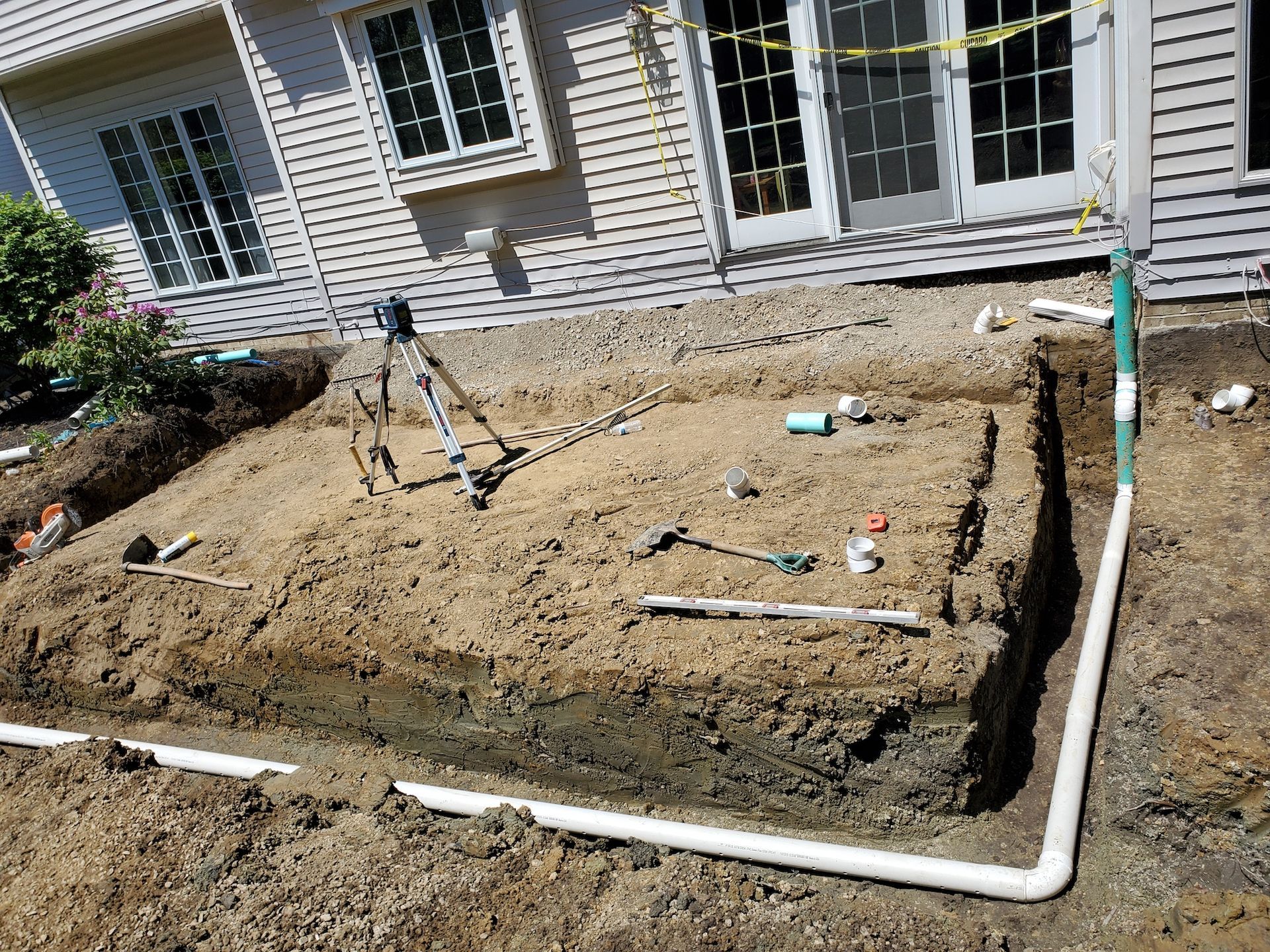 A drainage system is being installed in the dirt in front of a house.